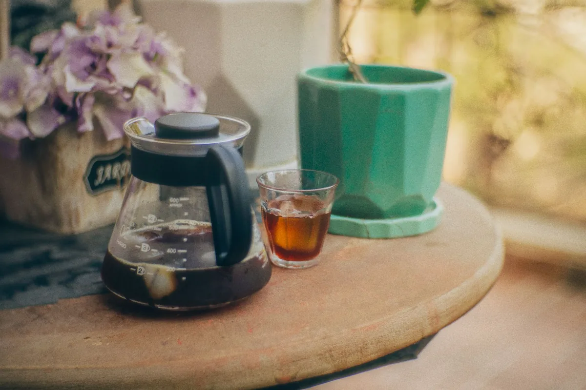 A glass carafe of coffee beside a green mug