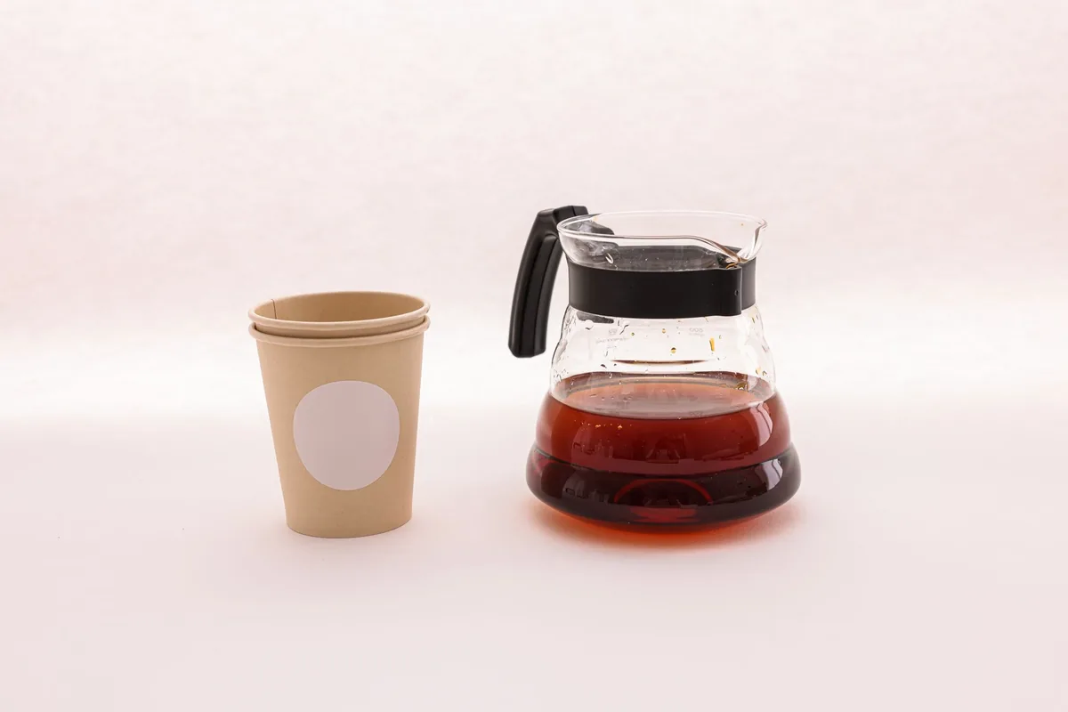 A glass carafe of coffee beside a single paper cup