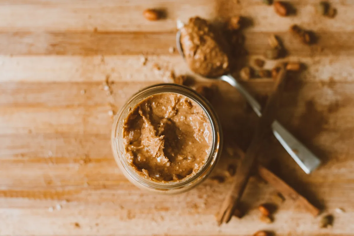 A glass jar of smooth homemade almond butter beside scattered whole almonds