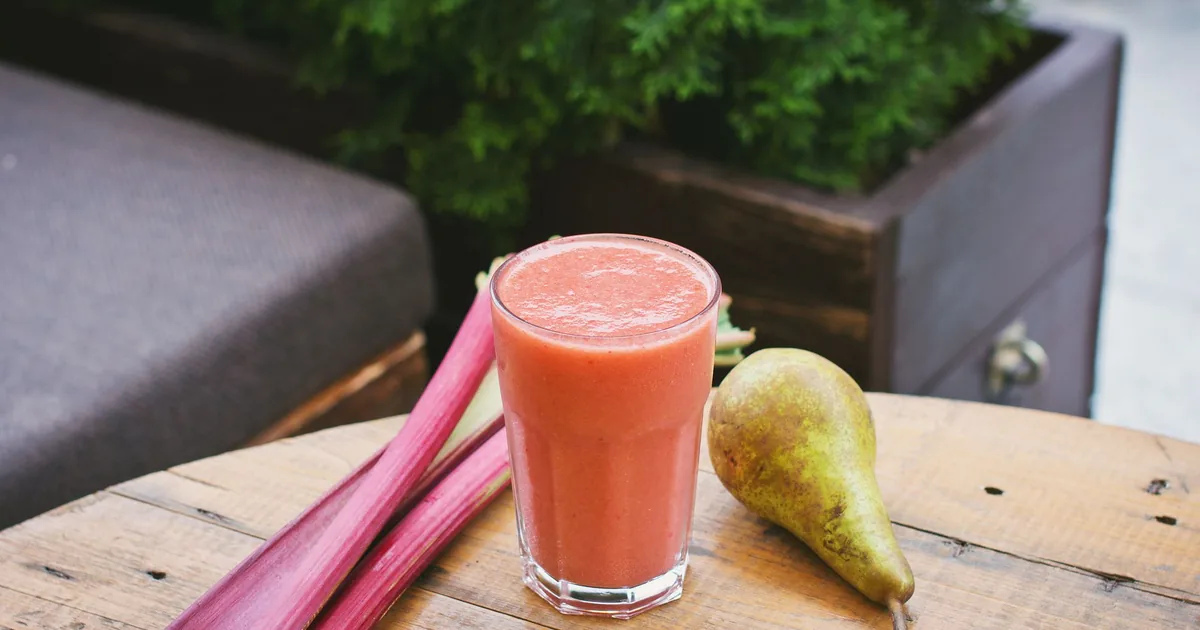 A glass of red smoothie beside a pear on a table