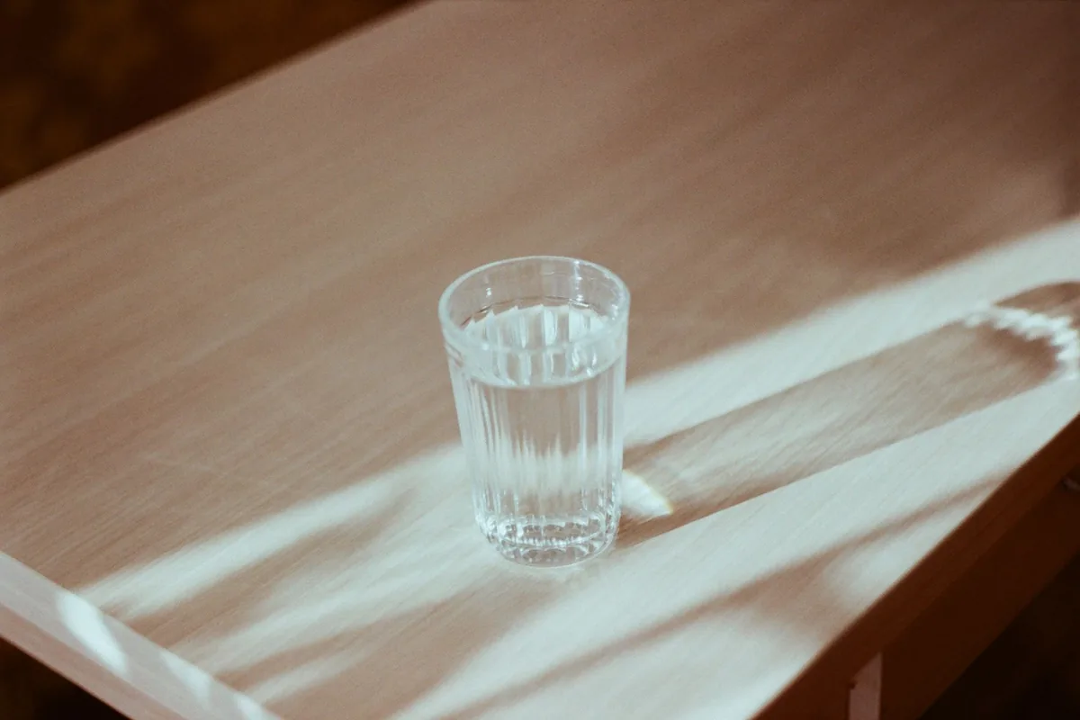 A glass of water on a sunlit wooden table