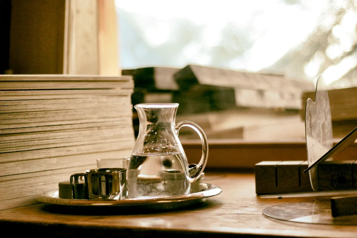 A glass water jug and cups on a tray on a wooden table
