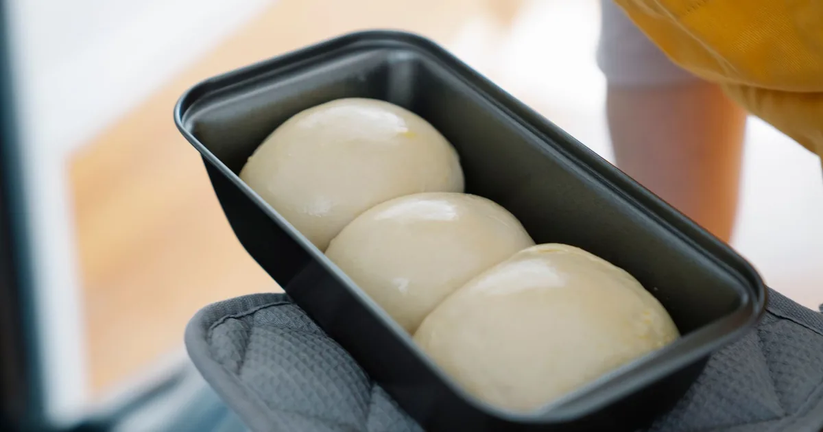 A golden domed loaf of bread sitting in a metal loaf pan on a light wooden worktop