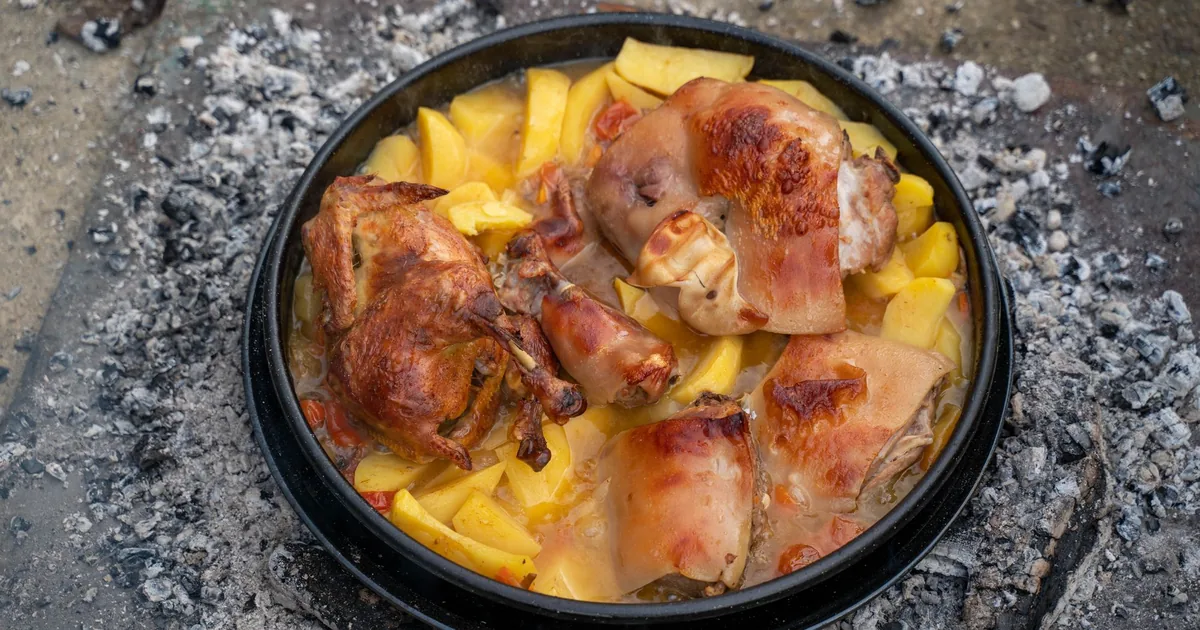 Roast chicken and potatoes in a dark pan over embers