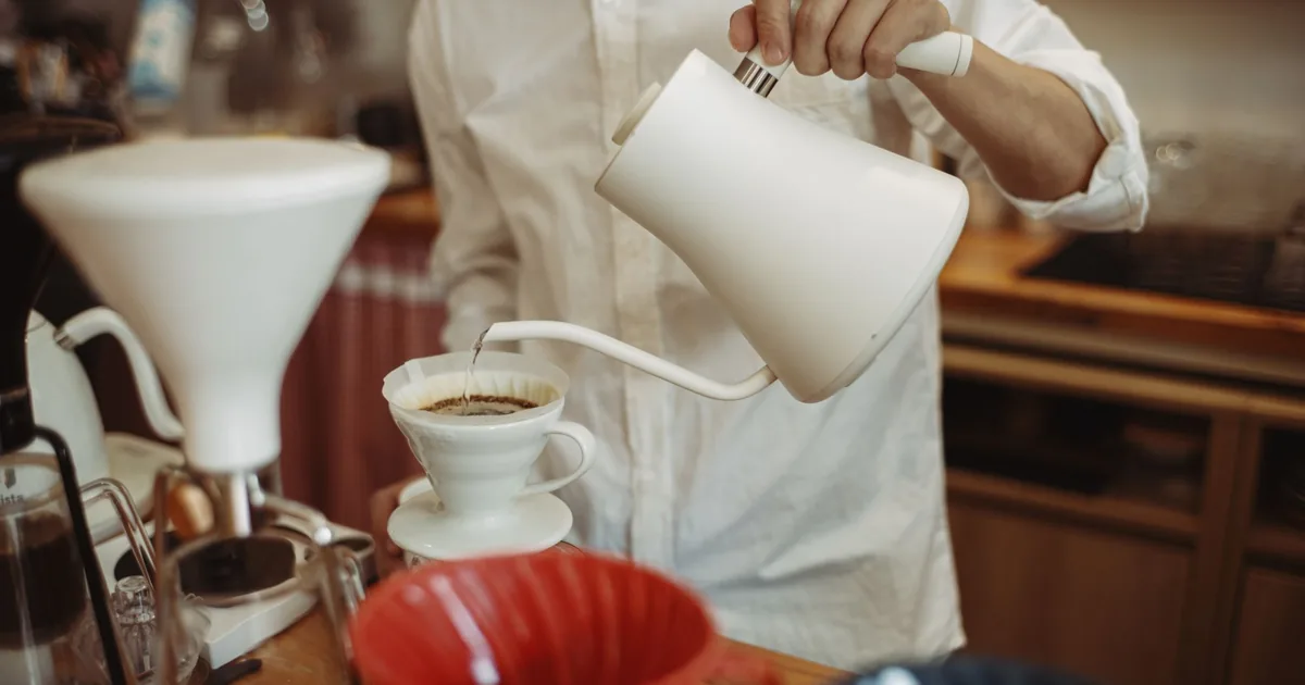 A gooseneck kettle pouring a thin stream of water into a pour-over coffee dripper