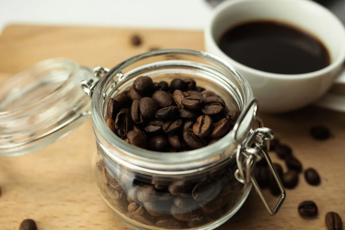 A jar of coffee beans beside a cup of black coffee