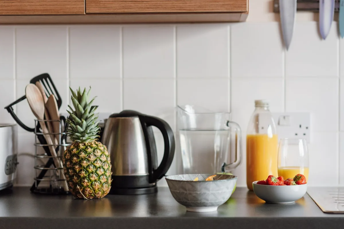 A kitchen counter with utensils, a kettle and fresh fruit