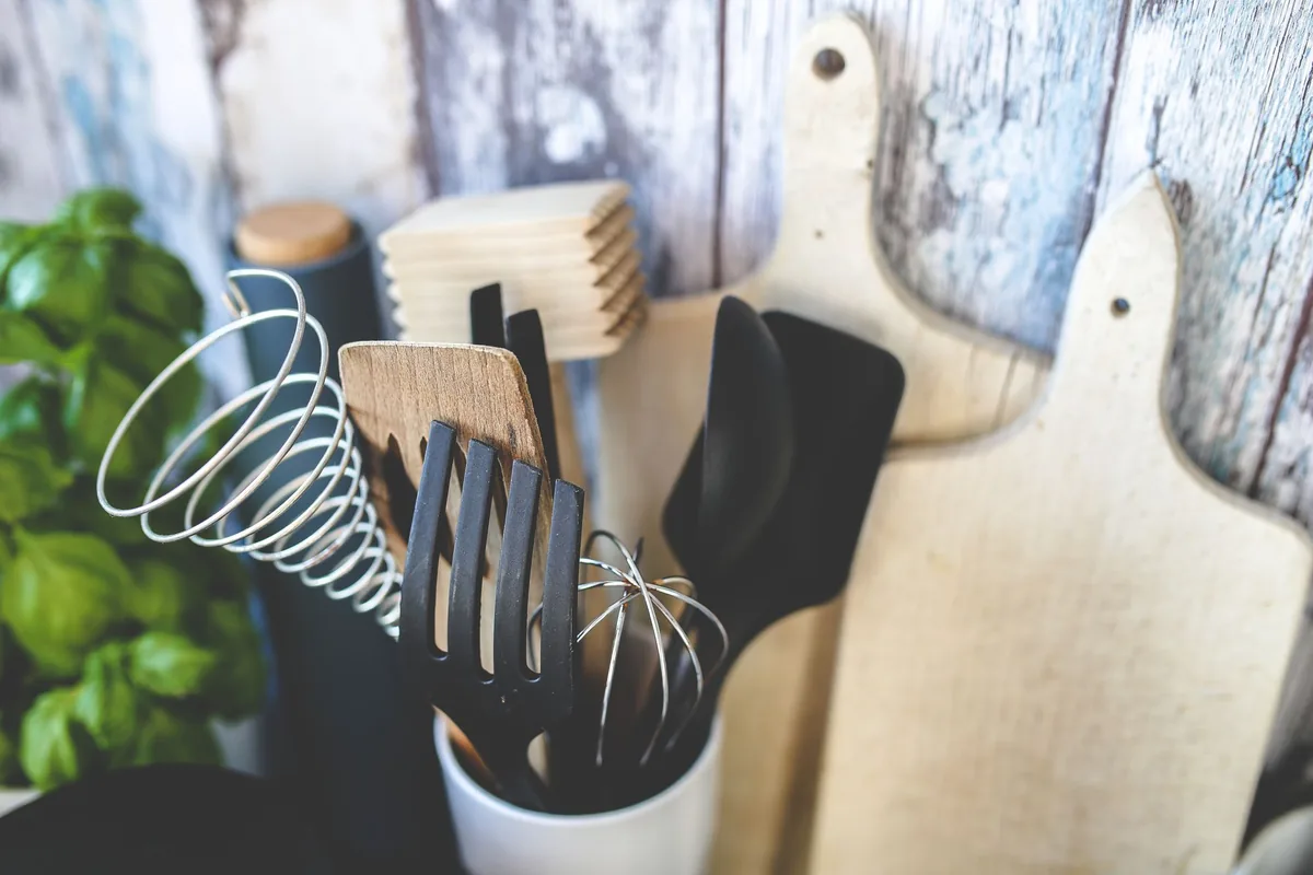 A ladle, a slotted spatula and a whisk laid side by side on a pale surface