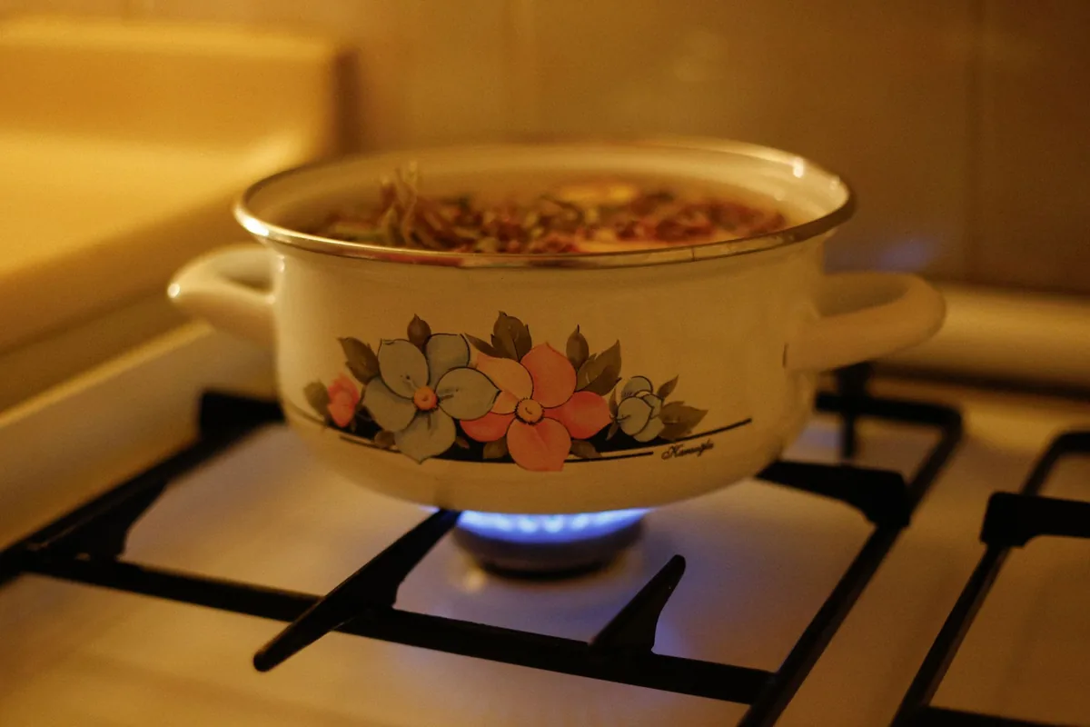 An enamelled pot with a floral pattern on a lit gas burner