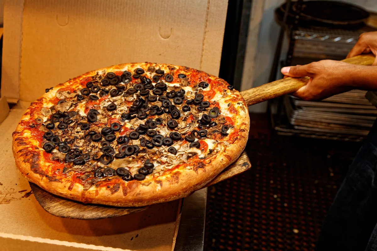 A large round pizza resting on a wooden peel on an outdoor table