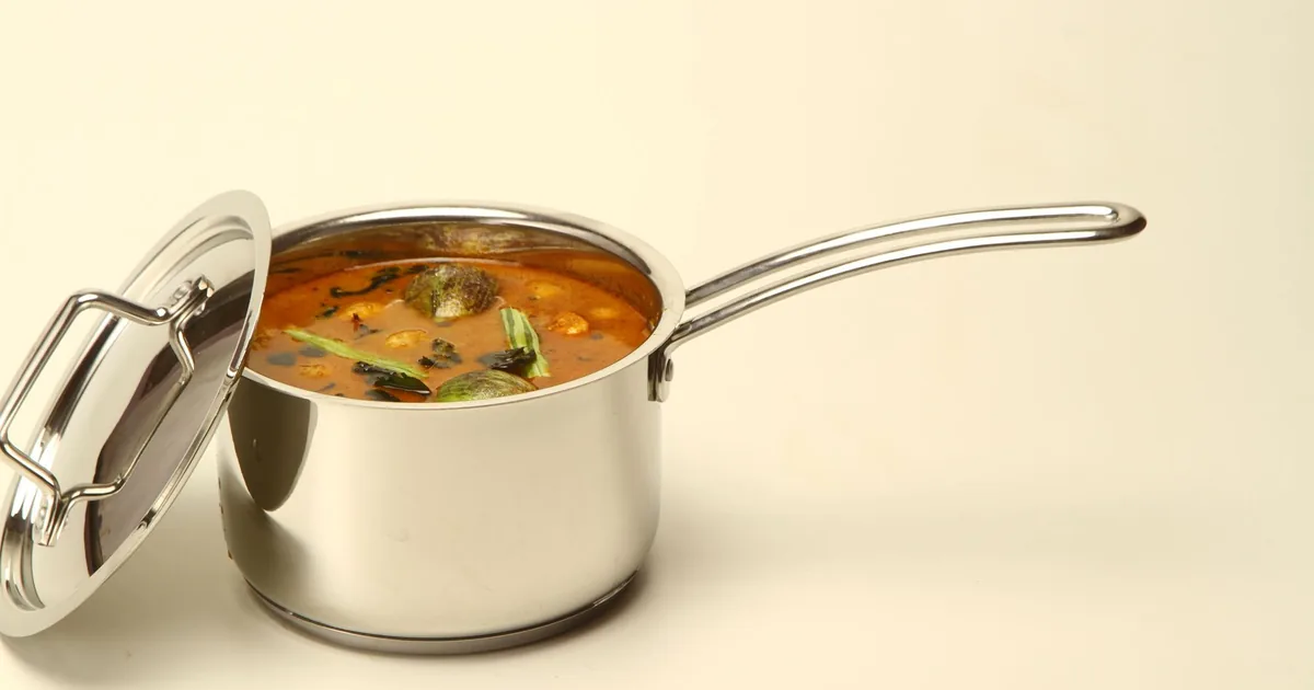 A lidded stainless saucepan of soup on a cream background