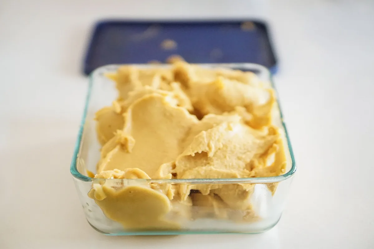 A loaf tin of pale homemade ice cream with scoop marks across its surface