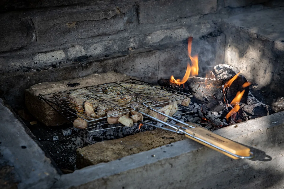 A long-handled grill basket resting over an open fire