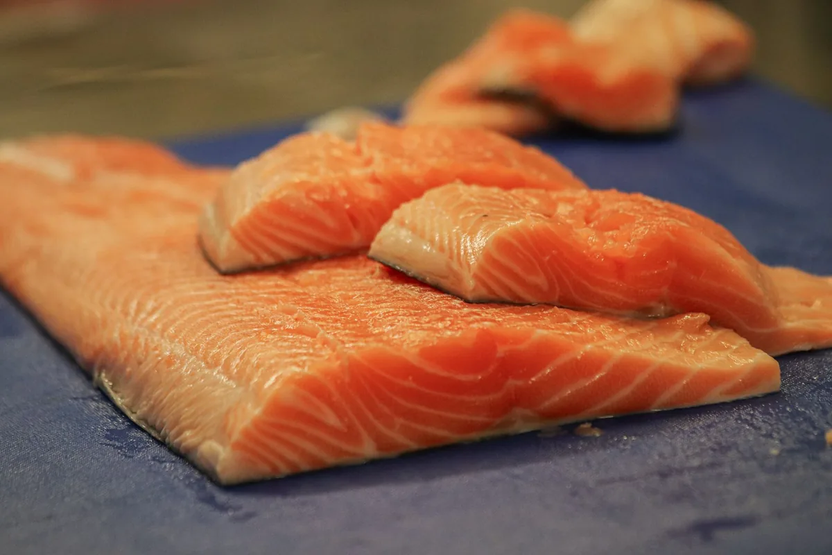 A long raw salmon fillet with its skin on lying on a pale chopping board