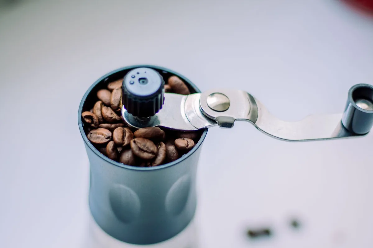 A manual coffee grinder beside a scattering of roasted coffee beans