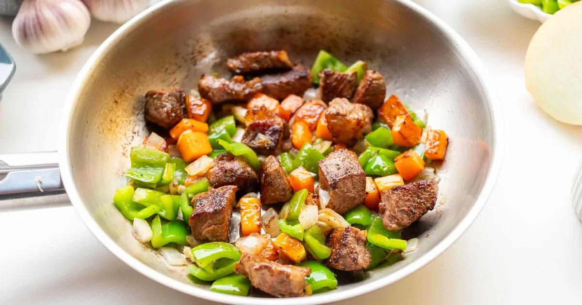 Beef and peppers cooking in a stainless steel pan