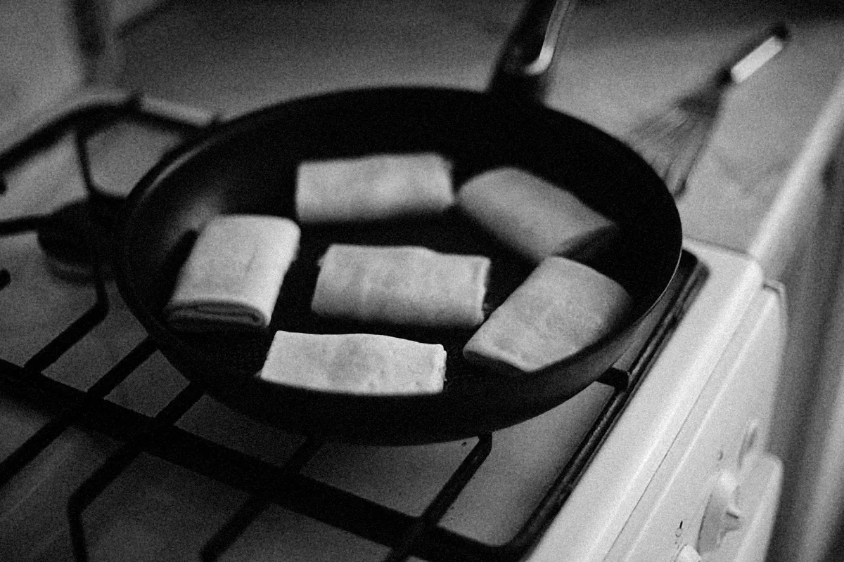 A black frying pan of dumplings on a gas stove grate, in black and white