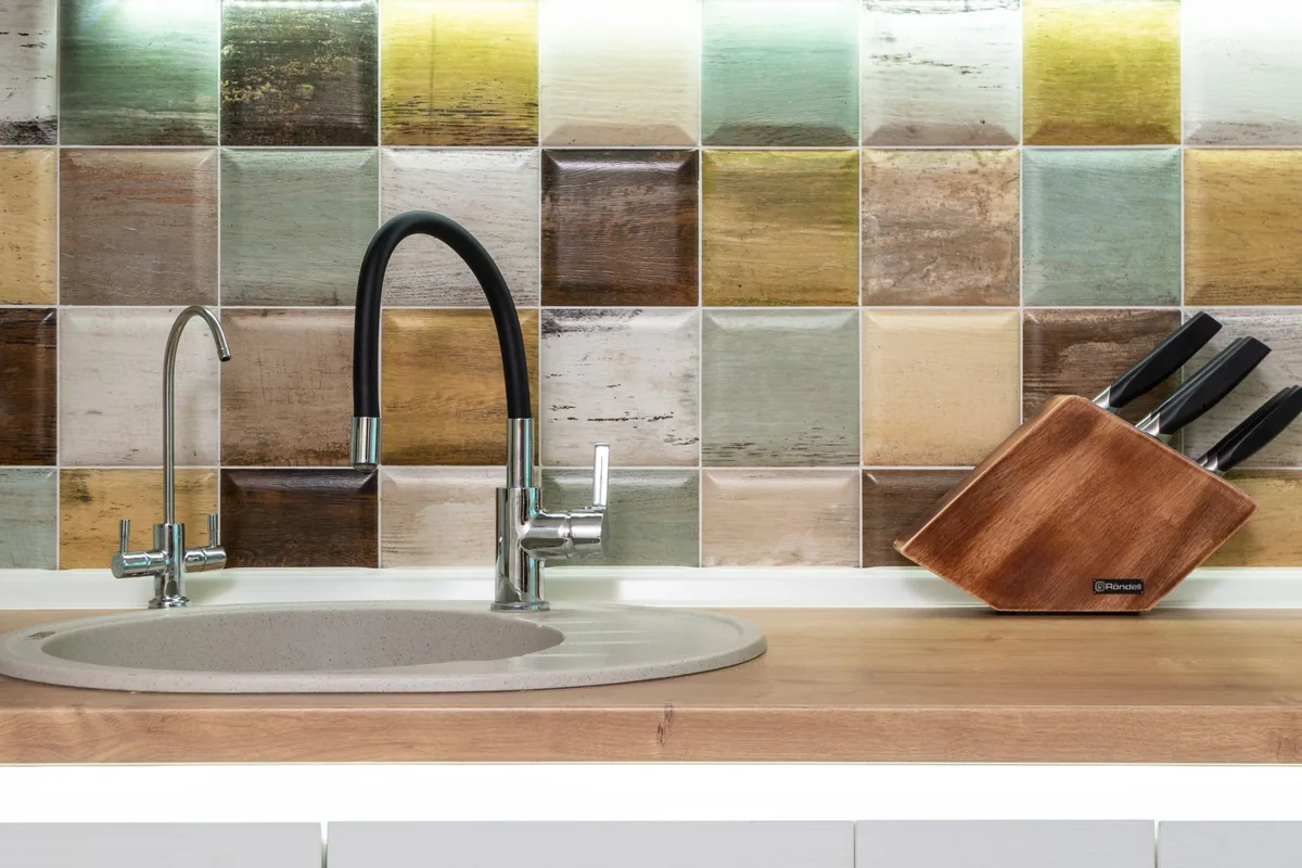 A modern kitchen sink with a tall stainless faucet and a bright window behind it