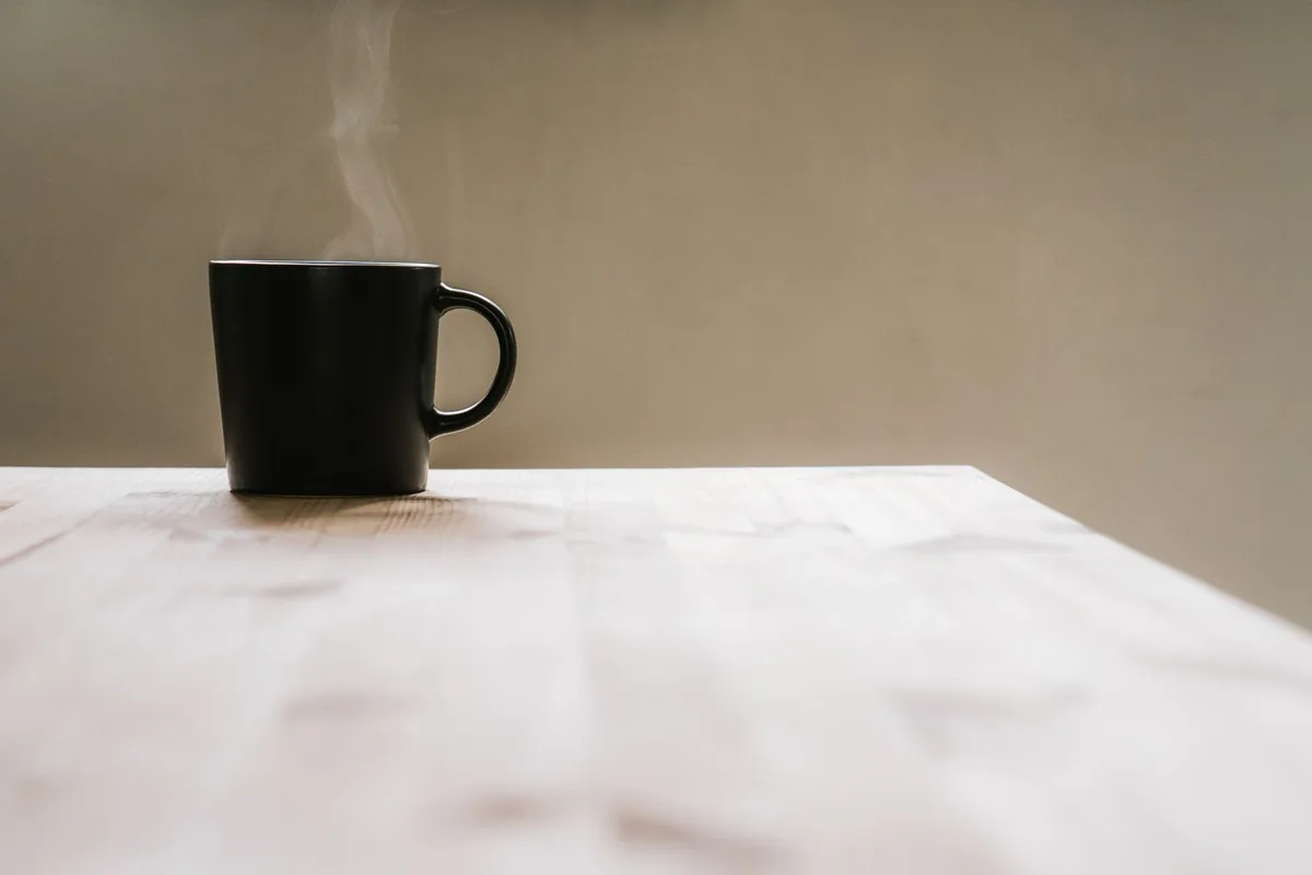 A mug of black coffee with steam rising from it in morning light