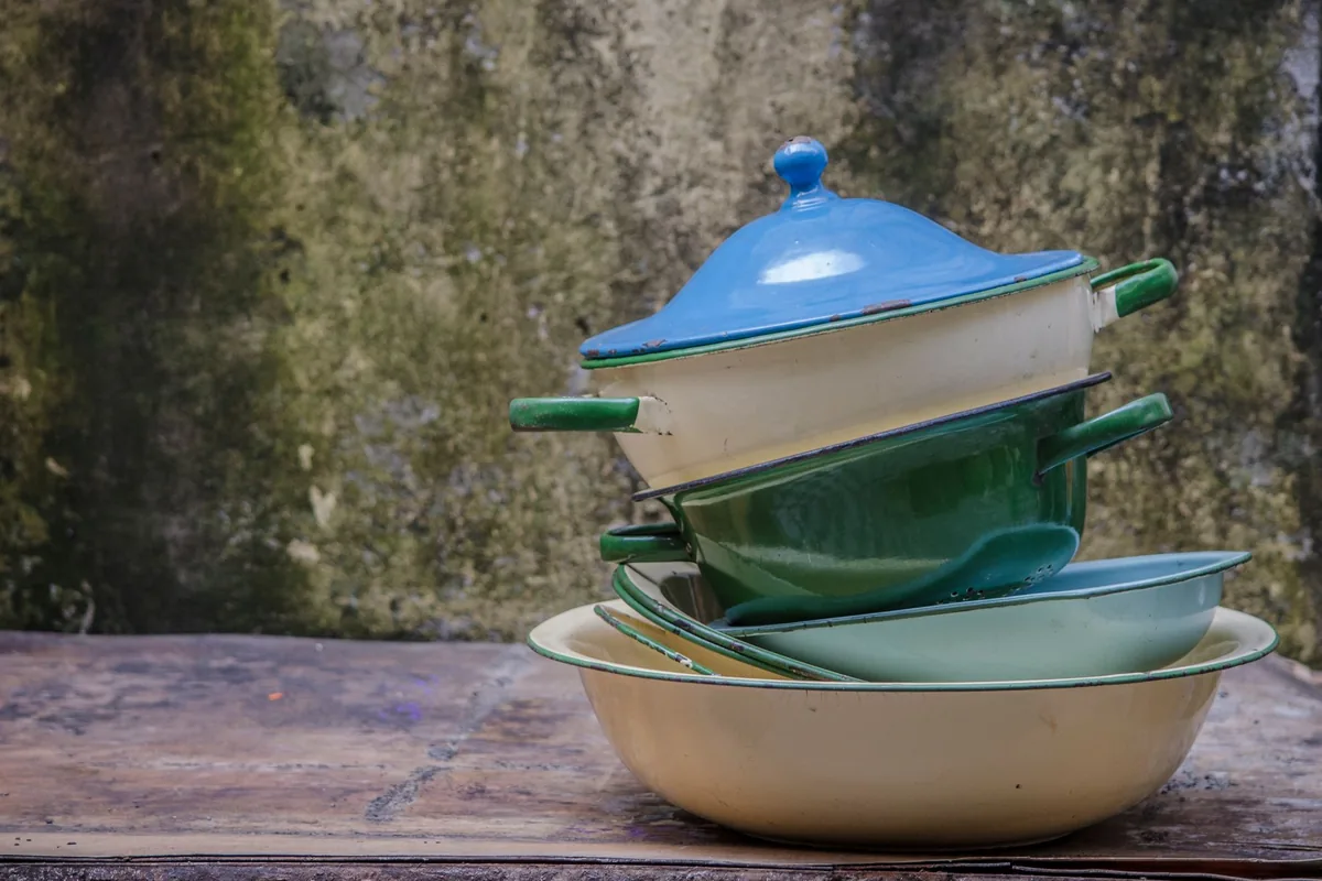 A neat stack of cooking pots and pans of different sizes on a white shelf