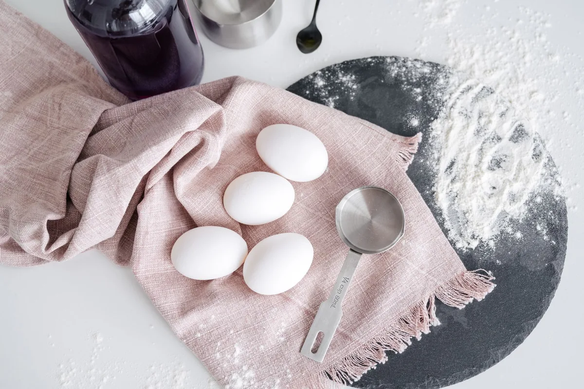 Eggs and a measuring cup on a pink cloth with flour