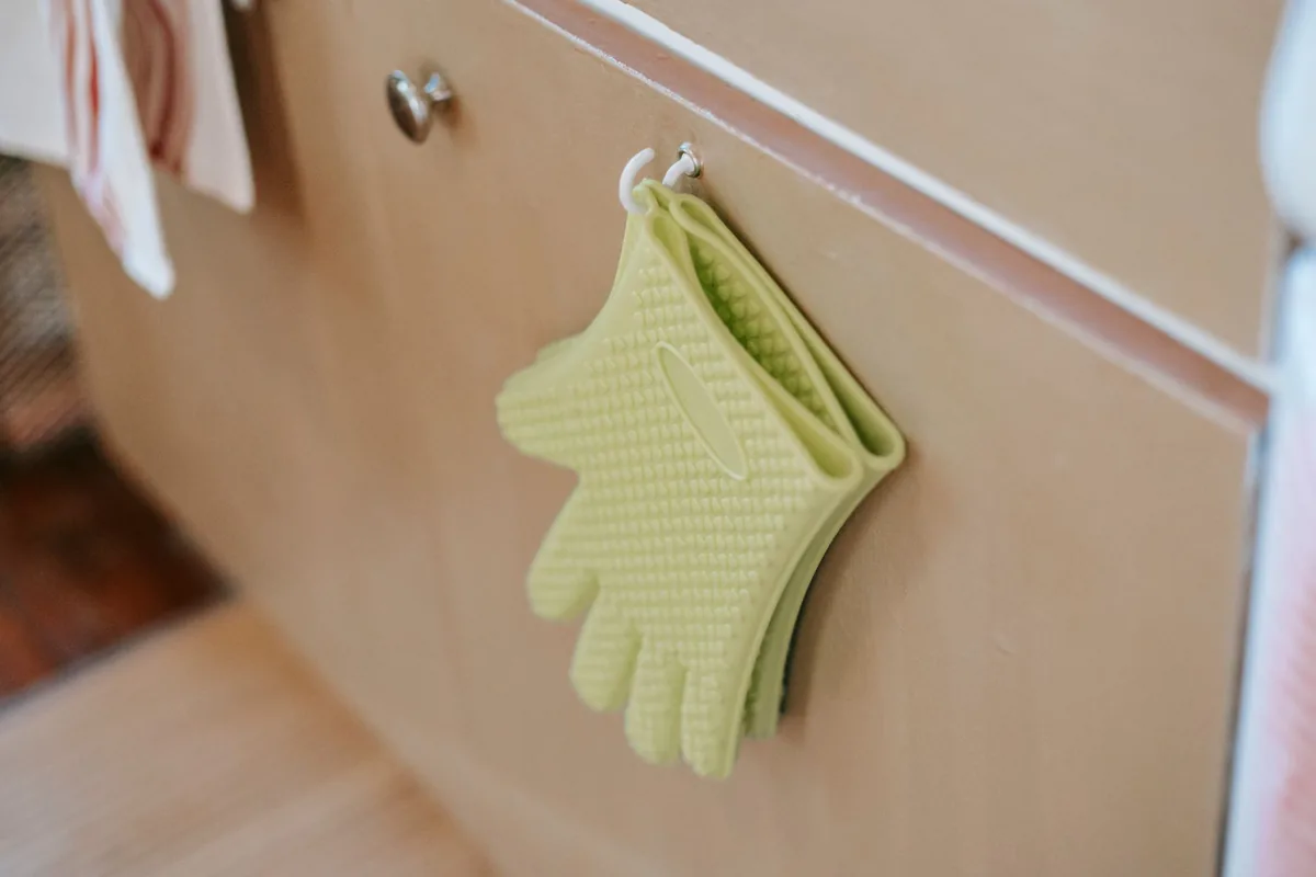 A pair of green silicone oven mitts hanging from a kitchen hook