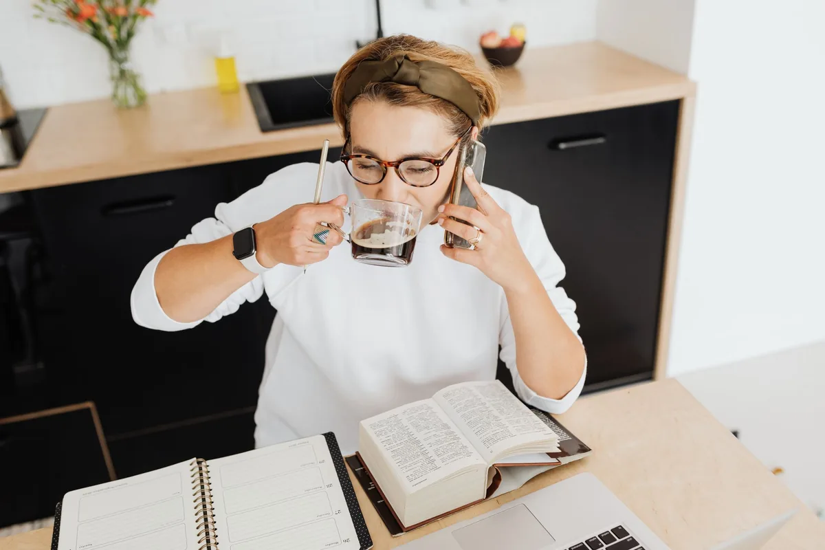 A person scrolling on a phone beside a cup of coffee