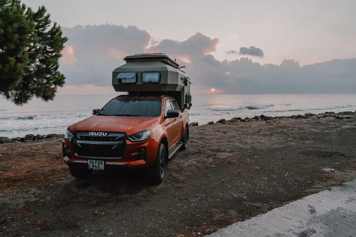 A pickup truck with a camper shell parked by the sea