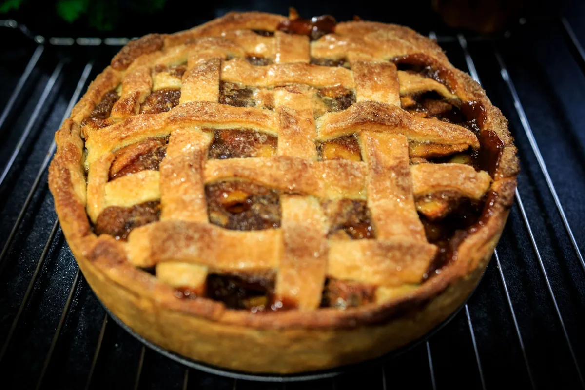 A pie with a browning crust on an oven rack seen through the open door