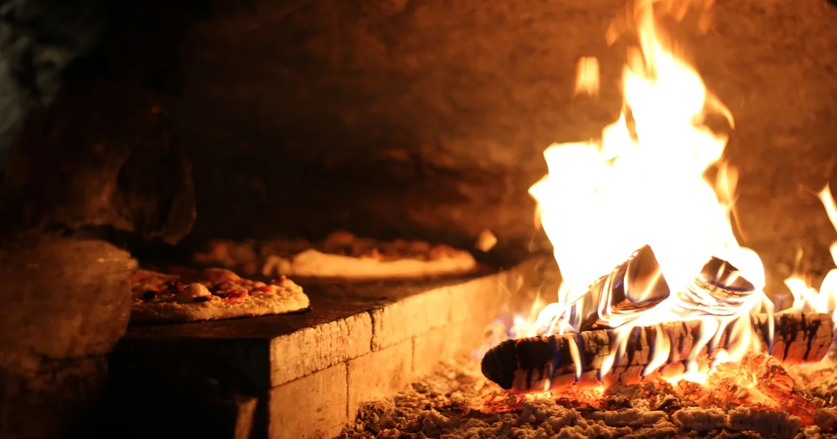 A pizza baking in front of a gas flame in a portable outdoor oven on a patio table