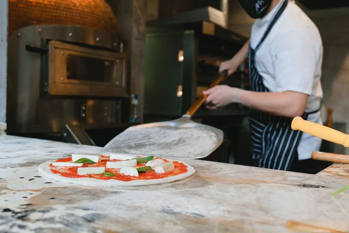 A pizza being slid into a hot outdoor oven on a peel
