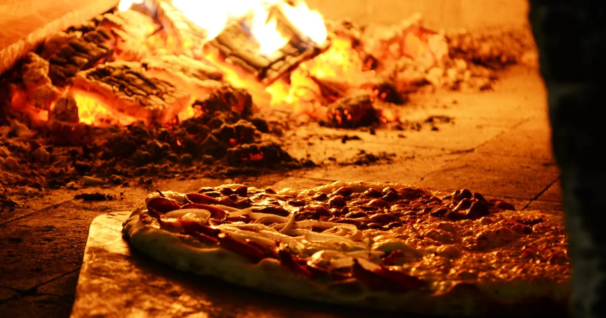 A pizza baking beside a wood fire in an oven