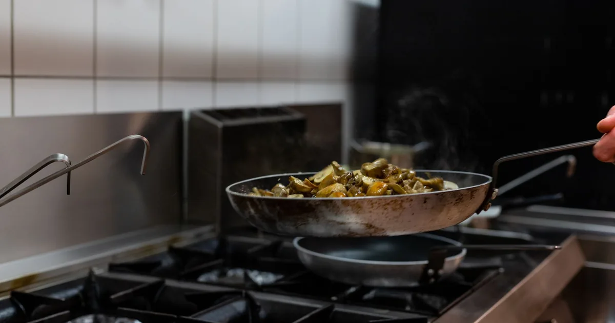 A polished stainless steel frying pan sitting on a stovetop burner in a bright kitchen