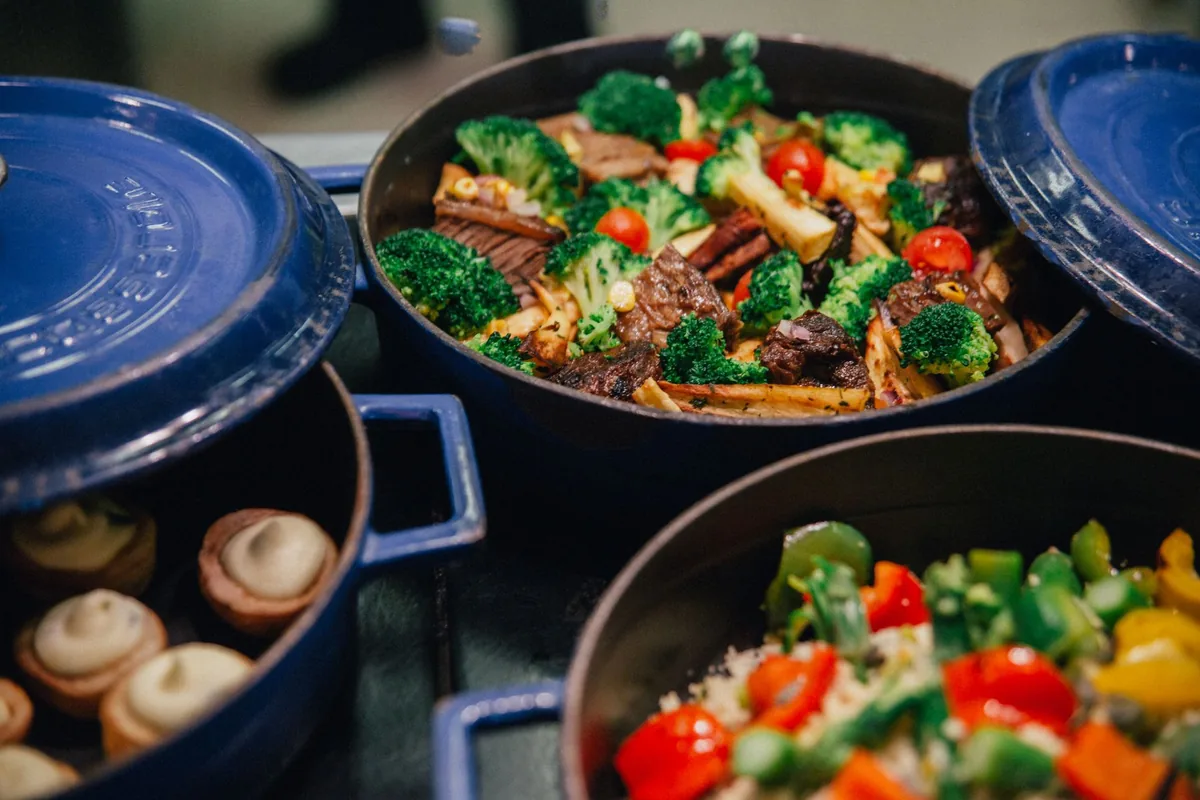 Blue enamelled cast iron pots filled with roasted vegetables and braised meat