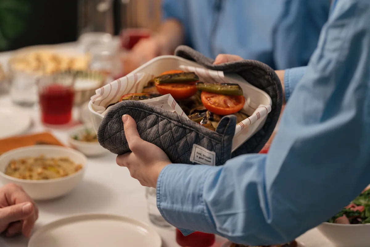 A quilted oven mitt holding a hot dish at a dining table