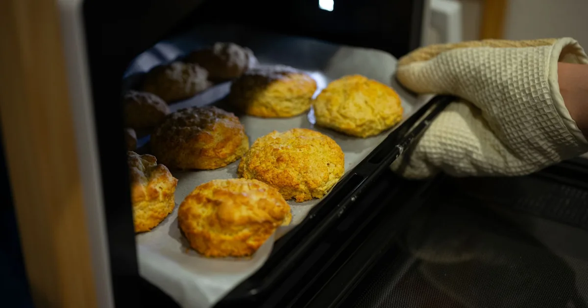 A quilted oven mitt lifting a tray of baked pastries out of an oven