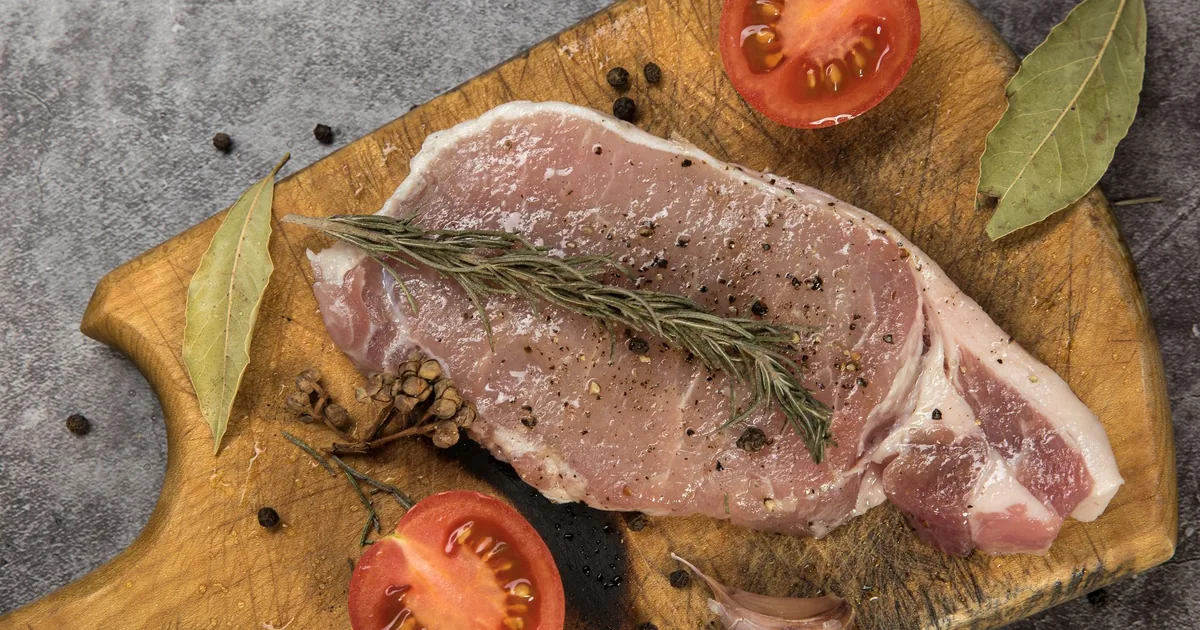 A raw pork steak with rosemary and tomatoes on a wooden board