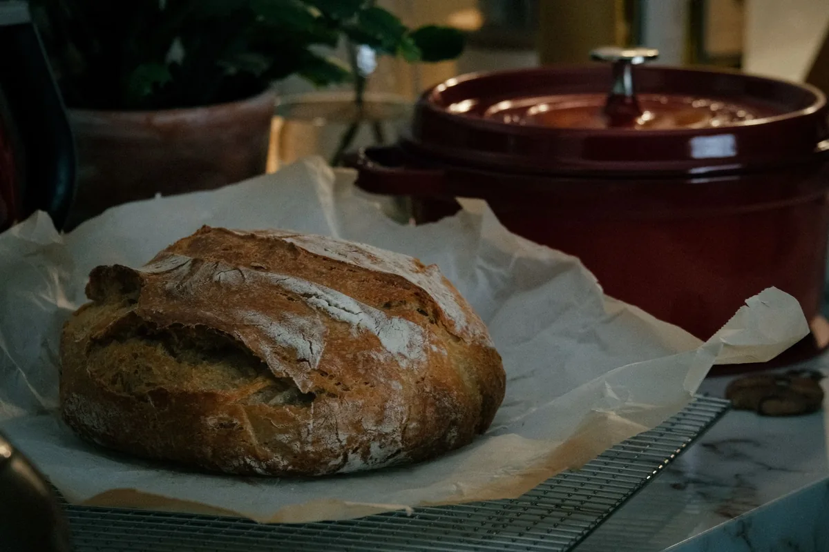 A red pot beside a round loaf on baking paper