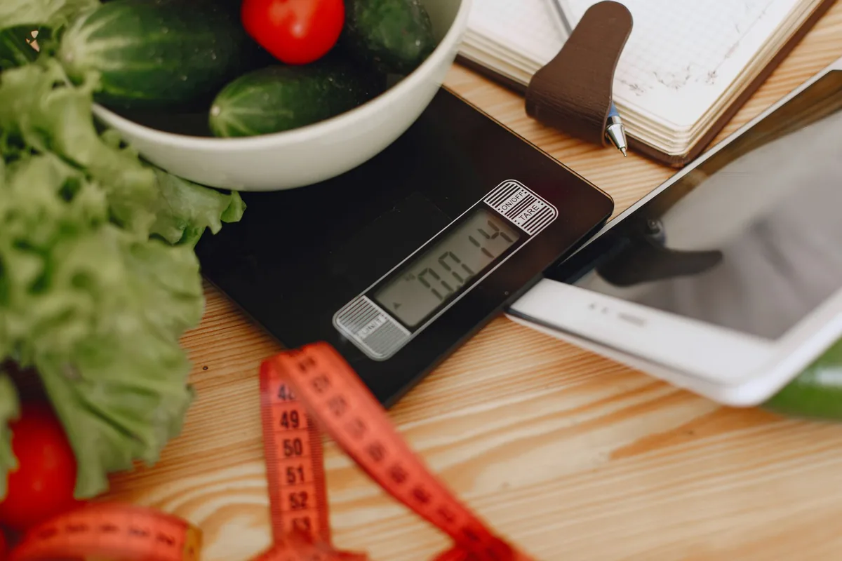 A kitchen scale, a tape measure and fresh vegetables on a wooden worktop
