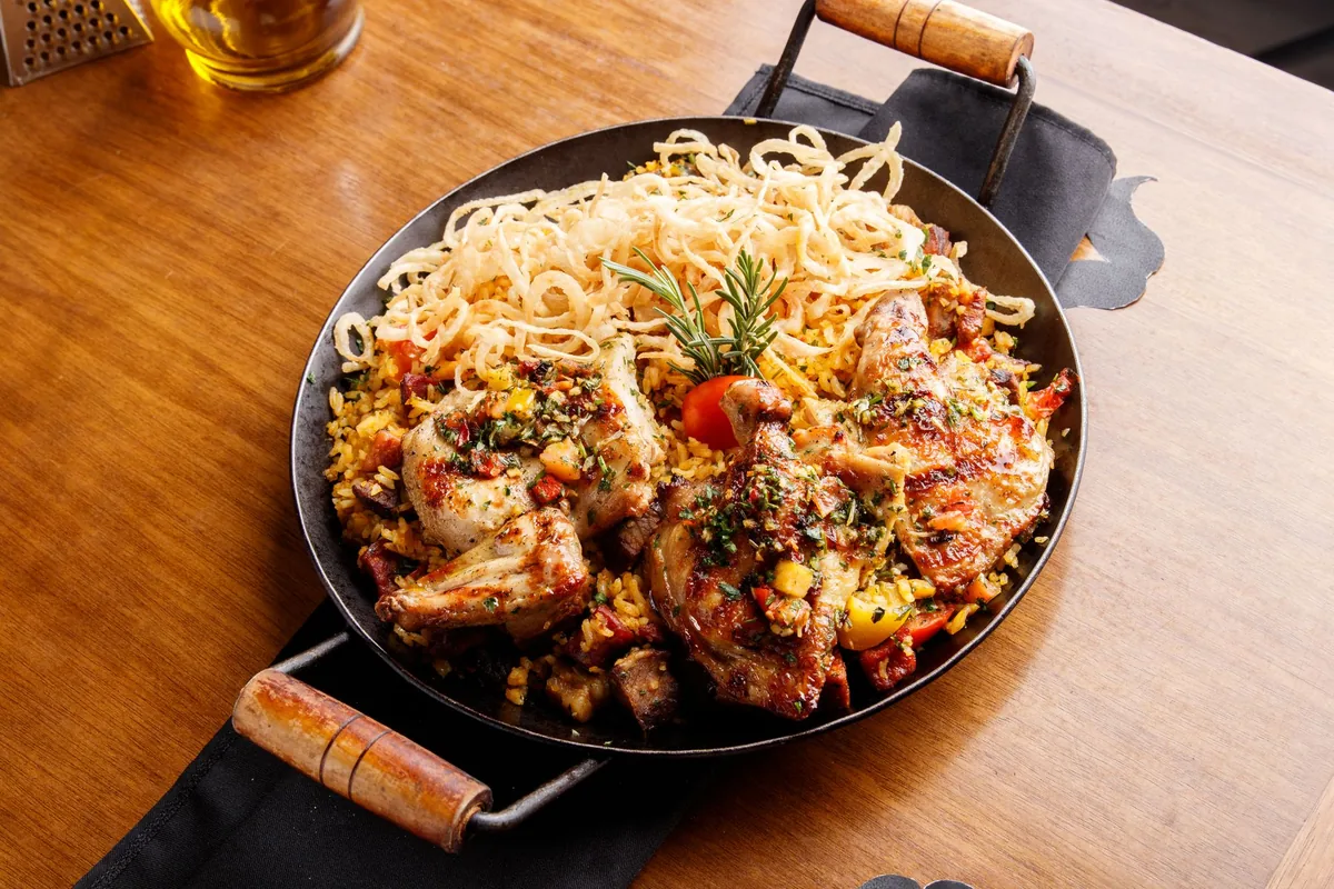 Noodles and chicken in a wide pan with wooden handles