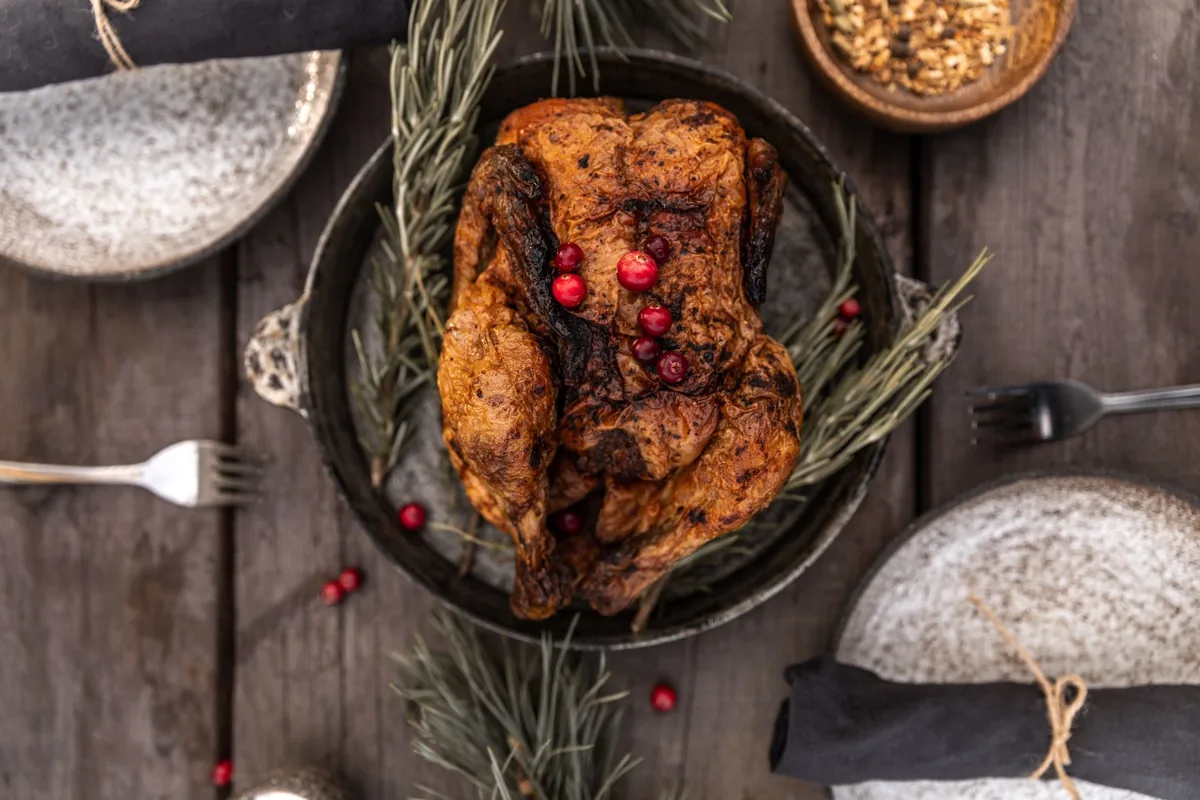 A roast chicken with herbs in a dark pan on a wooden table