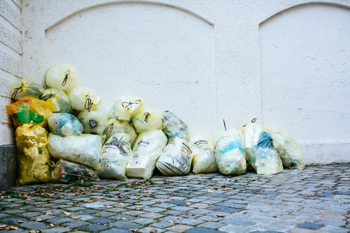 Bags of rubbish piled against a white wall