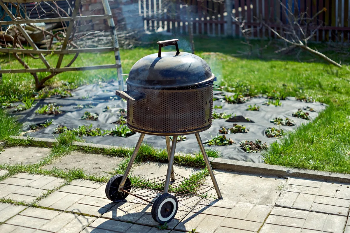 A round kettle grill with its lid closed standing on a paved garden patio