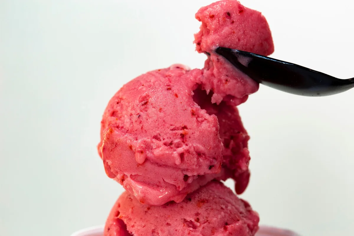 A scoop of pink strawberry sorbet in a small dish with fresh strawberries beside it