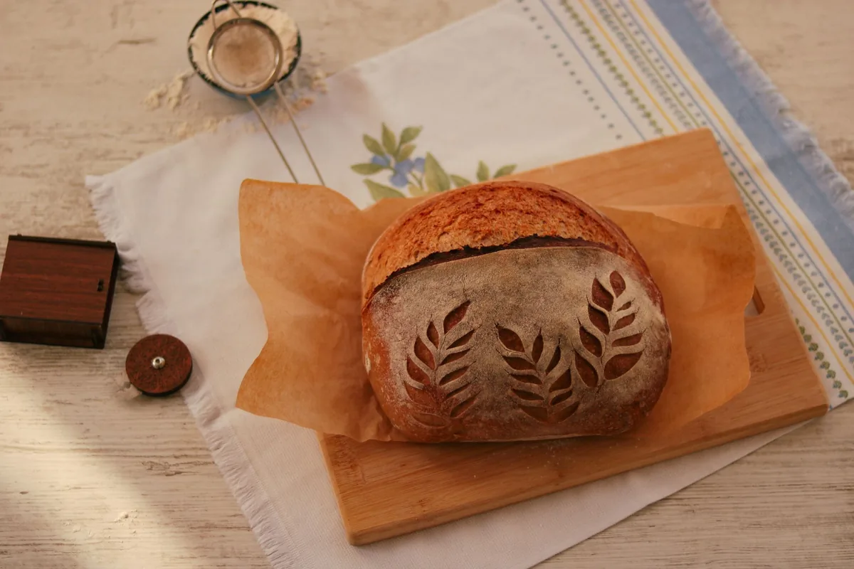 A scored round sourdough boule on parchment paper before baking