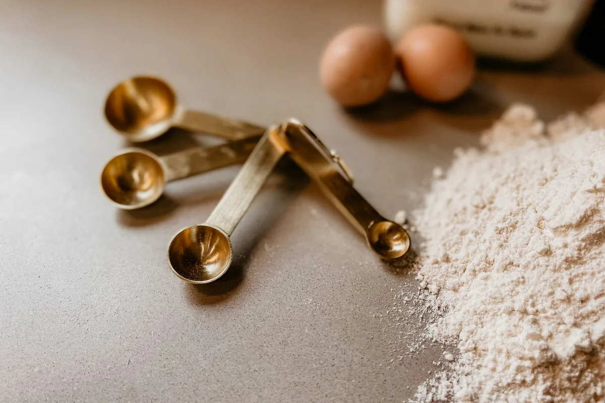 Gold measuring spoons beside flour and eggs