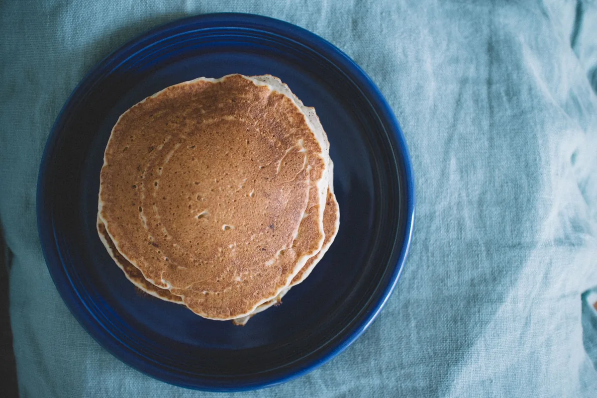 A single golden pancake on a blue plate resting on a linen cloth