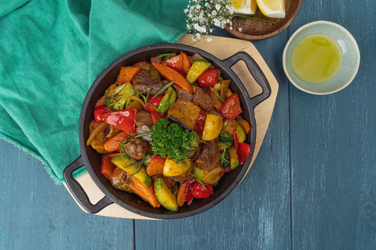 A skillet of colourful vegetable stew on a blue table