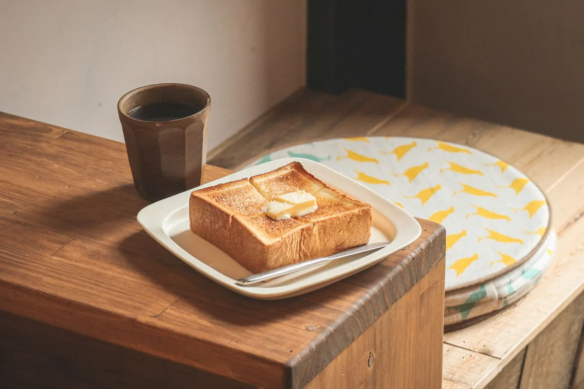 A thick slice of buttered toast on a plate beside a cup