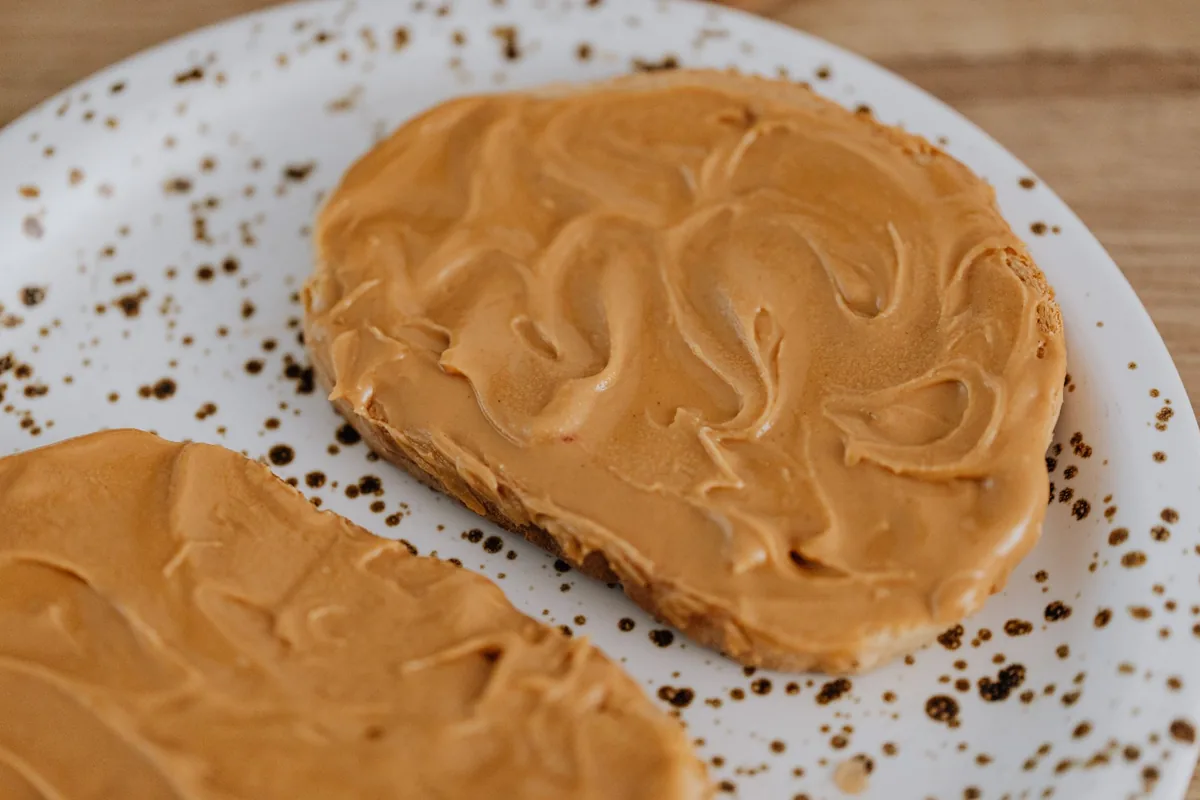 A slice of toast spread with smooth nut butter on a white plate